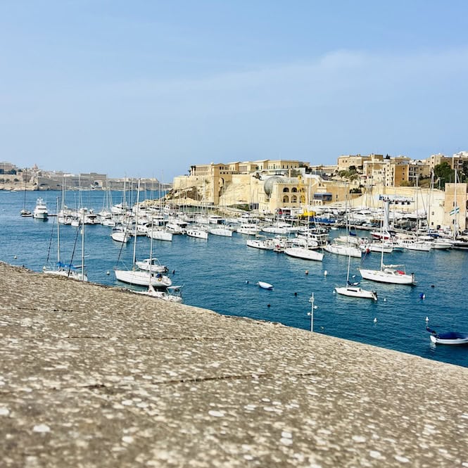 Numerous boats and yachts docked in the harbour of Malta's Three Cities, with historic buildings and fortifications lining the waterfront.