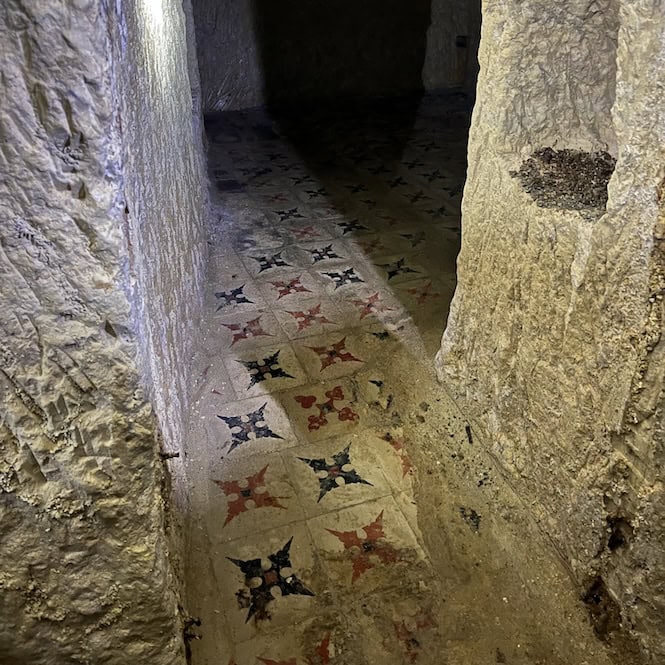 A small room in Underground Valletta with carved-out windows and colorful tiles on the floor.