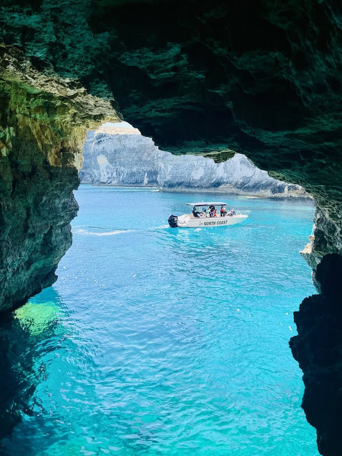 A boat carrying passengers visible through a cave opening on Comino's coast, an impressive sight along the hiking trail.