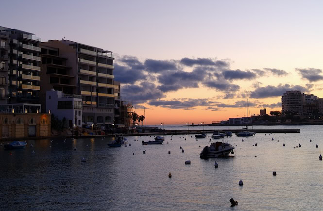 Spinola Bay in St. Julian's, Malta, is a vibrant and scenic spot known for its excellent restaurants and lively nightlife. The bay is lined with modern buildings, restaurants, and cafes, offering a variety of dining options and nightlife venues. Small boats are moored in the calm waters, adding to the picturesque charm of this popular area.