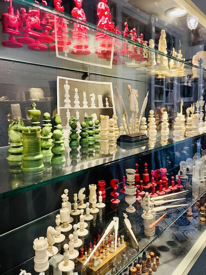 Glass display case showcasing various chess sets in red, green, and white colors, along with other decorative items.