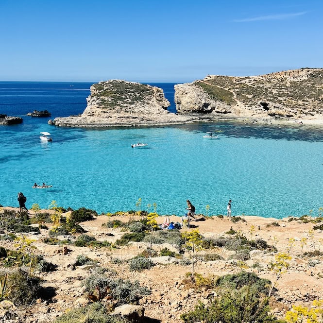 Stunning turquoise waters of the Blue Lagoon in Comino, Malta. Popular tourist attraction with rocky coastline, small boats, and visitors enjoying the crystal-clear Mediterranean Sea.