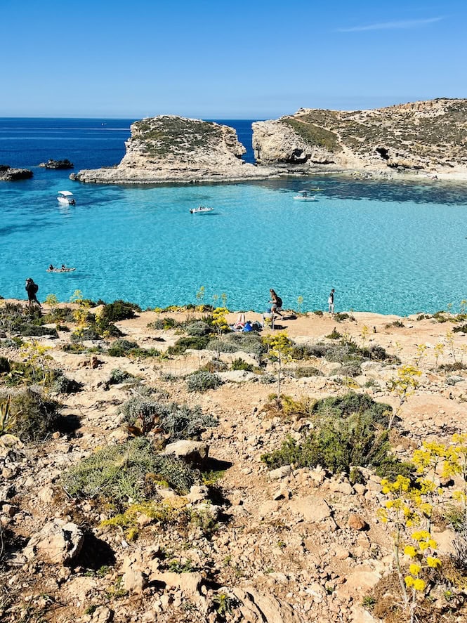 Breathtaking Blue Lagoon in Comino, Malta. Crystal-clear turquoise waters surrounded by rocky cliffs. Boats and swimmers enjoying the stunning natural beauty.