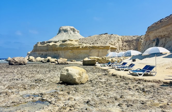 imestone cliffs and pebbly beach with sun beds at Xwejni Bay in Gozo