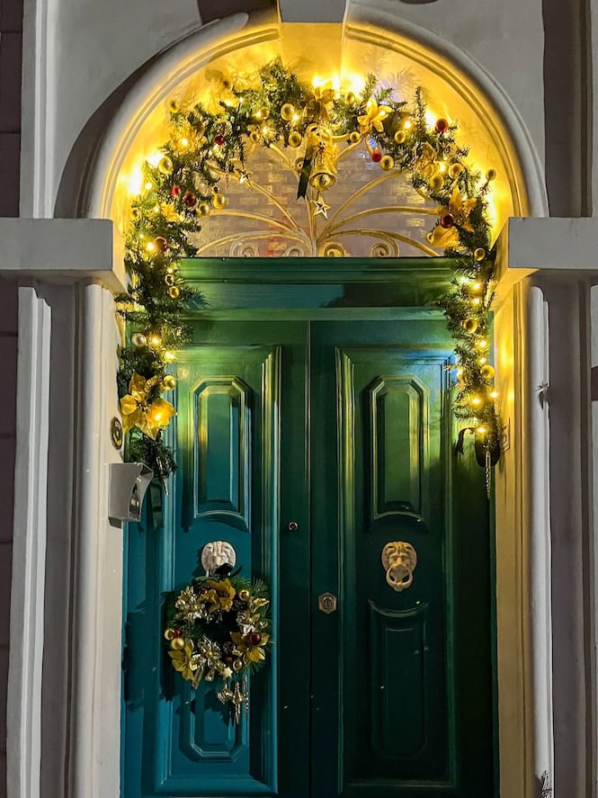 A beautifully decorated green door in Malta adorned with Christmas lights, a wreath, and golden ornaments, capturing the festive holiday spirit in a traditional Maltese home.