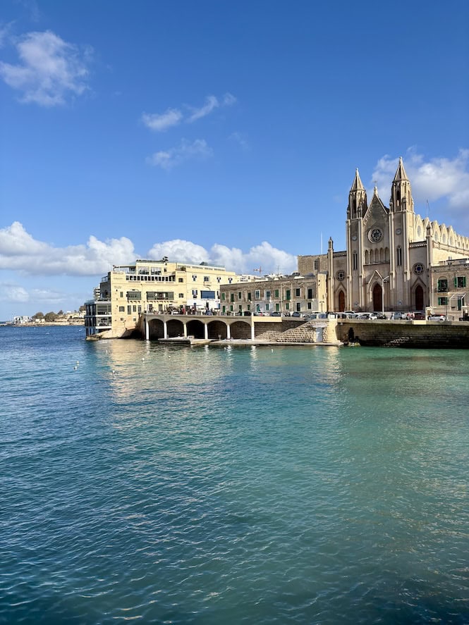 Neo-Gothic Carmelite Parish Church in Balluta Bay, Malta, with its stunning waterfront arcade reflecting in calm January waters under clear blue skies