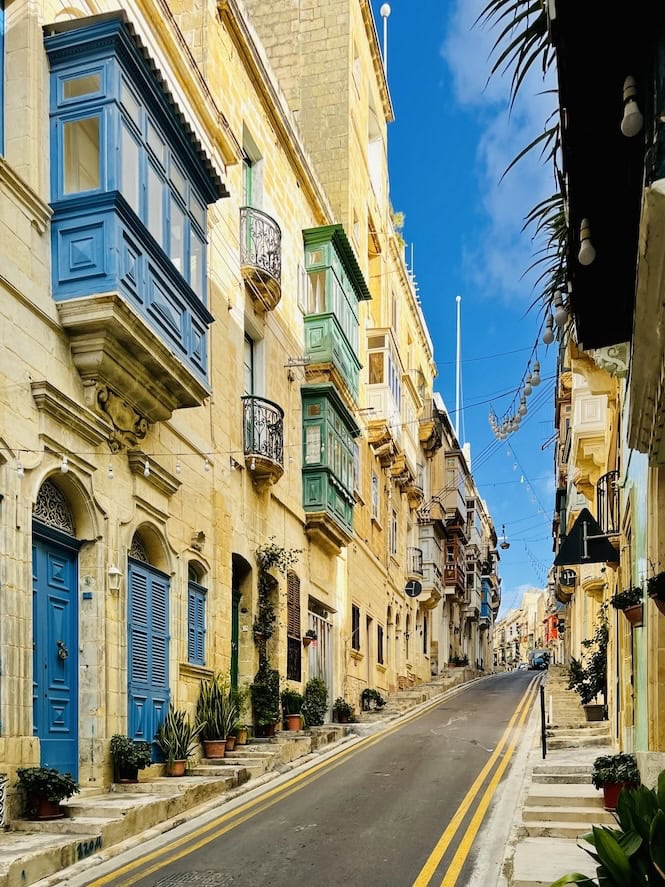 Traditional narrow street in Malta with colorful balconies and clear road markings, showcasing road safety measures in a historic urban setting.