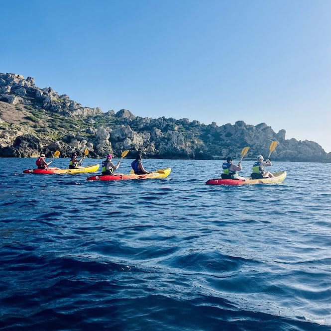 ourists kayaking along a rocky coastline under blue skies during summer in Malta.