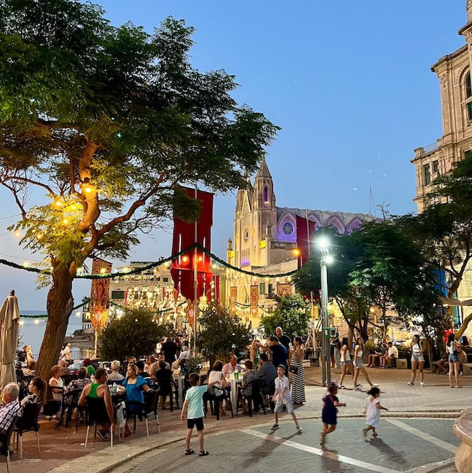 Locals and visitors enjoying the evening during summer in Malta, with lights and street decorations.