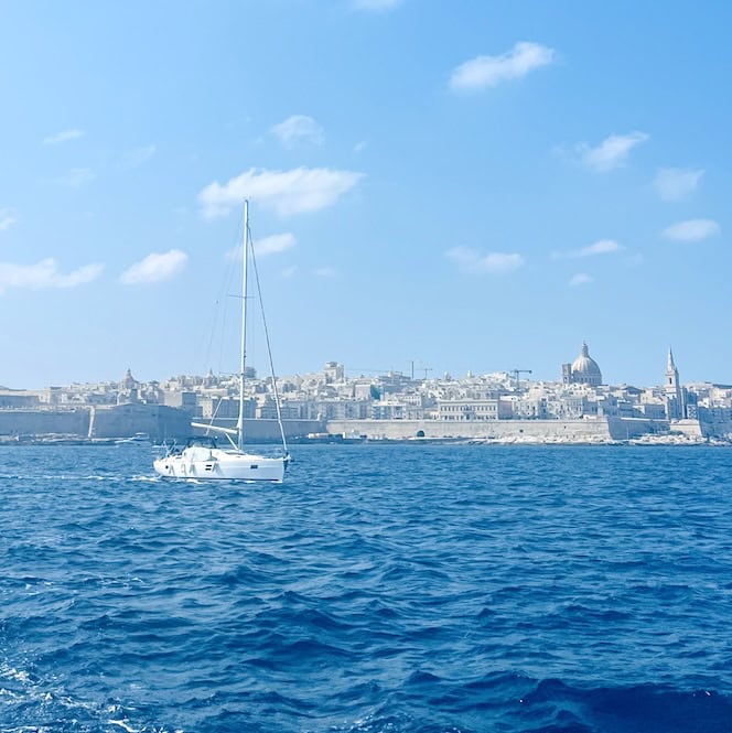 A white sailboat glides across the blue sea with Valletta in the background – one of the most romantic things to do in Malta for couples seeking a private boat experience.