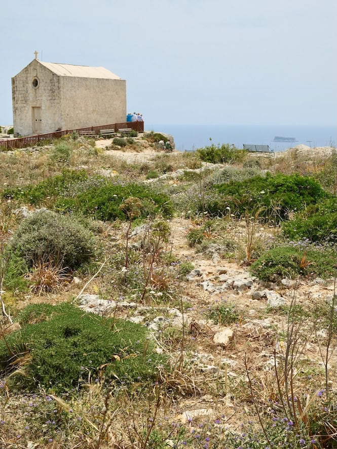 A small stone chapel sits near the edge of Dingli Cliffs in Malta, overlooking wild Mediterranean scrubland and the distant sea—showcasing one of the top free things to do in Malta.