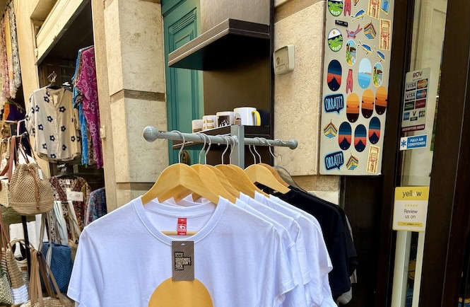 Street display of modern Maltese souvenirs including graphic T-shirts, stickers, and tote bags outside a local shop in Valletta