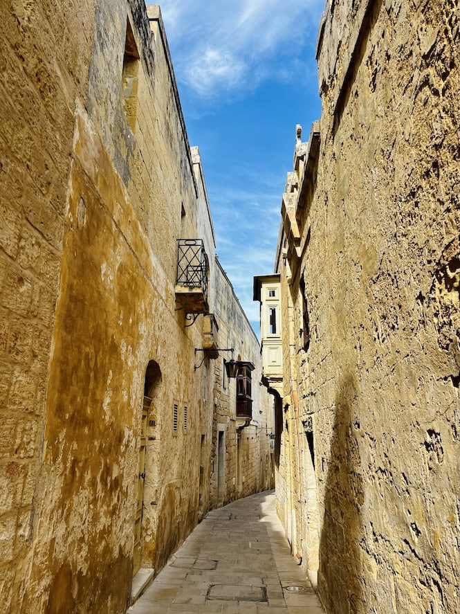 A sunlit narrow street with high golden limestone walls in Mdina, Malta, showing a quiet and historic alleyway—one of the best free things to do in Malta.