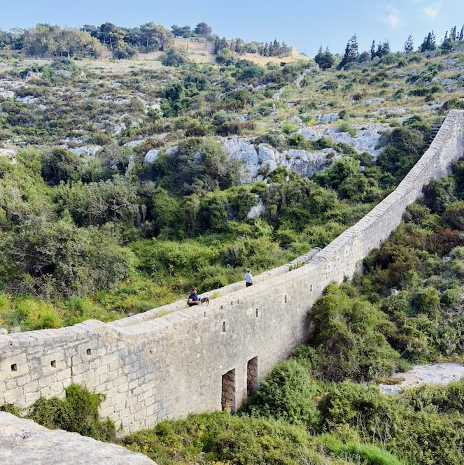 Two hikers sitting on top of the Victoria Lines defensive wall on the eastern section between Fort Madliena and Gharghur, Malta