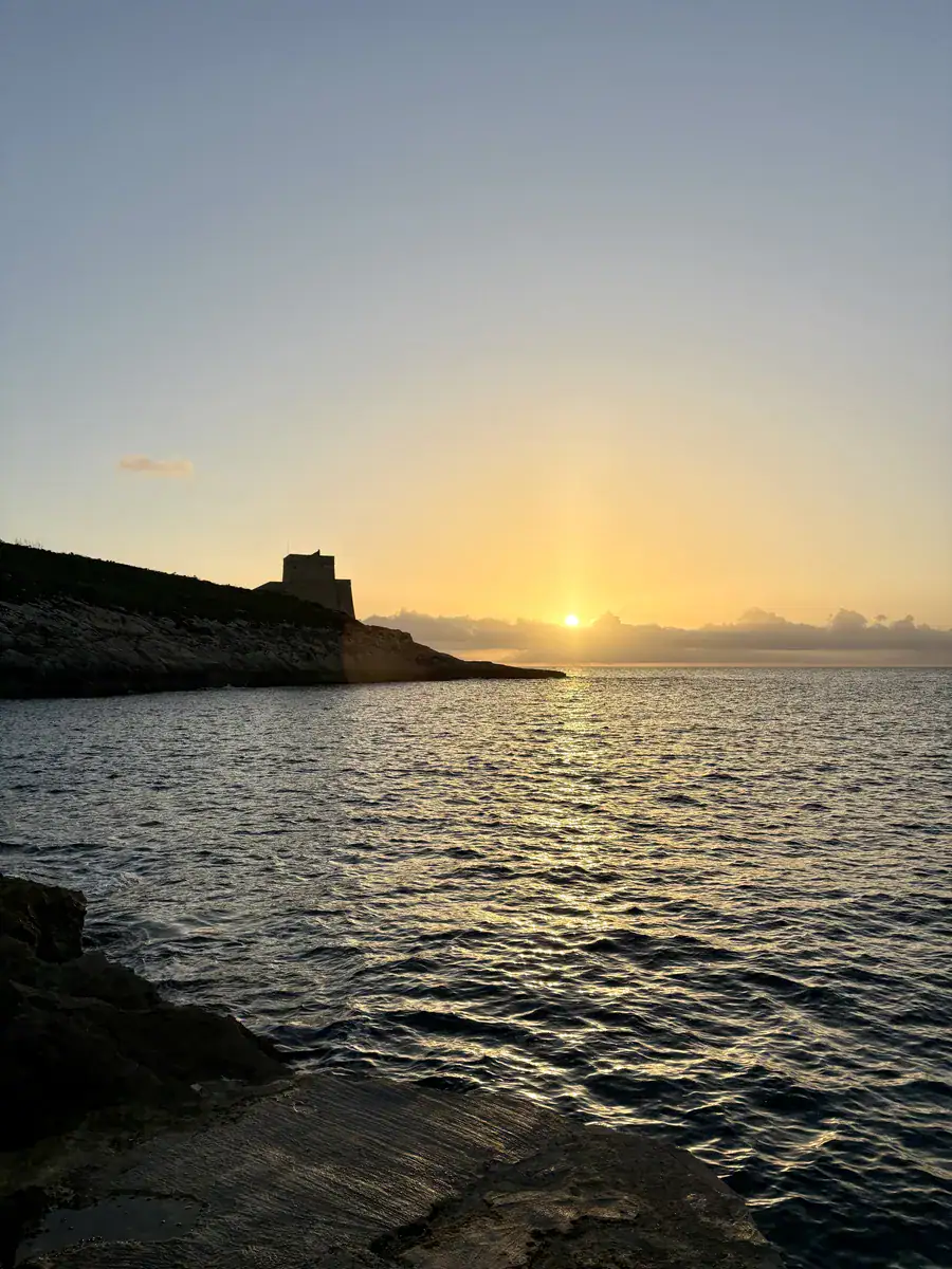 Sun setting over the sea next to Xlendi Tower, seen from the rocks in Xlendi, Gozo